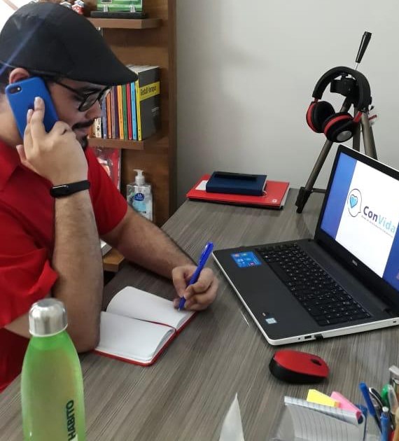 psicólogo sentado em frente a mesa falando ao telefone e escrevendo em caderno